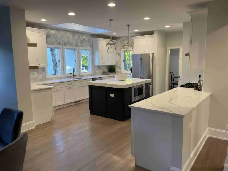 Sleek, contemporary kitchen design showcasing stainless steel appliances, white marble countertops, a large central island with bar stools, and pendant lighting over an open-plan layout.handyman kitchen renovation