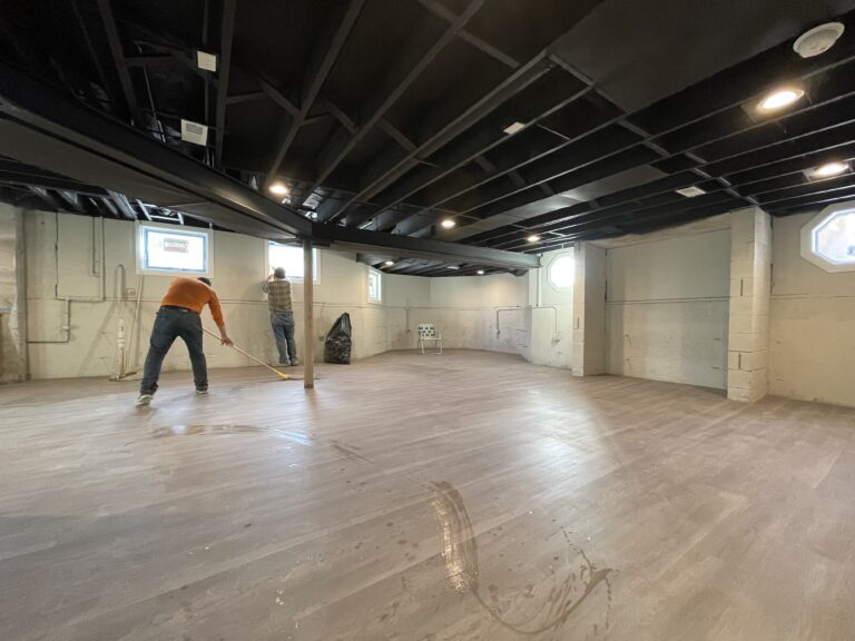 Work in progress on a wooden floor renovation, with a half-sanded surface showing the contrast between the old and the new finish.