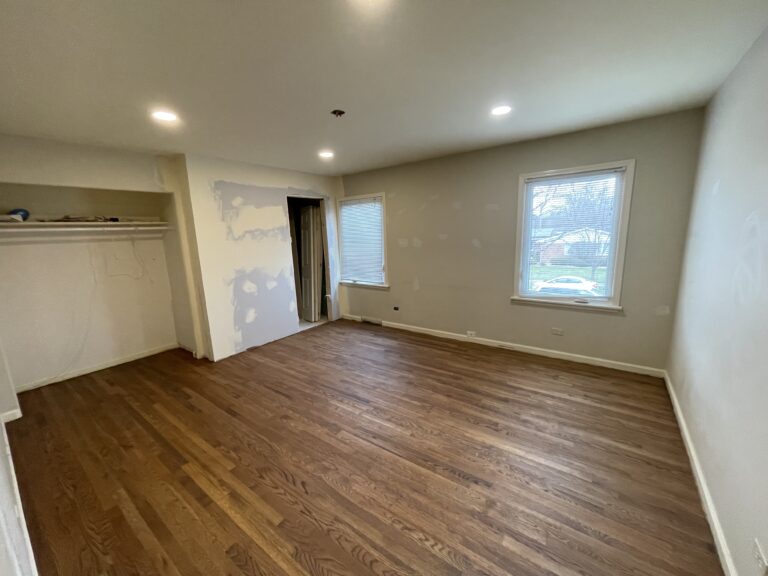 A spacious room undergoing wooden floor restoration, with tools and sanding equipment scattered around, illustrating the renovation process.