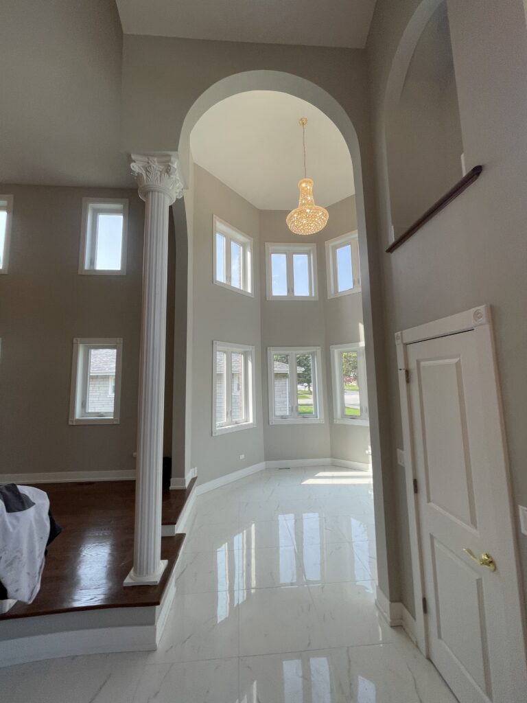 Elegant main entrance hall inside a house, showcasing grand columns, a high ceiling with a statement chandelier, polished marble floors, and a sweeping staircase leading to the upper level, creating a luxurious and welcoming ambiance.